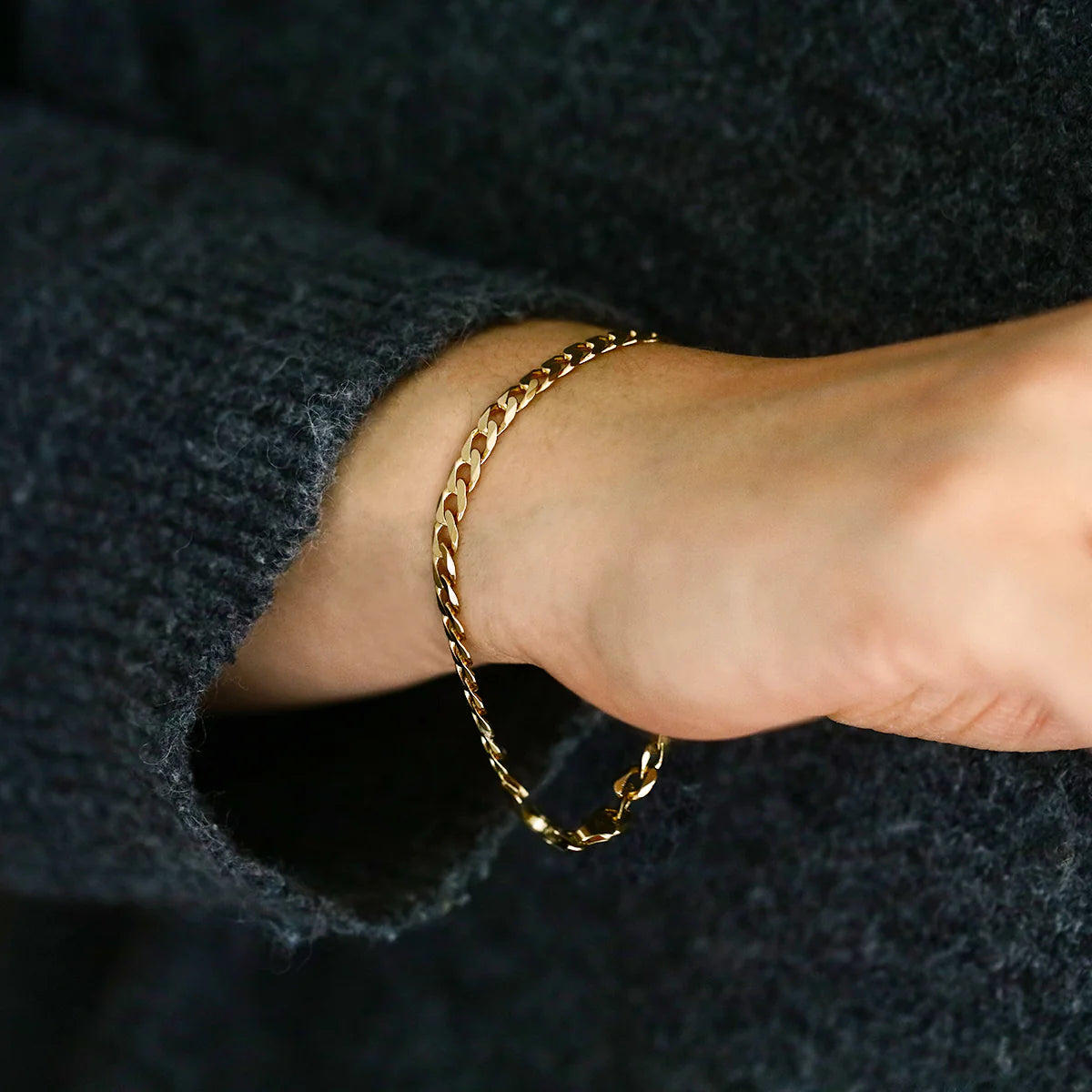 Gold chain bracelet on a wrist with a dark background available on the TX.ORO website.