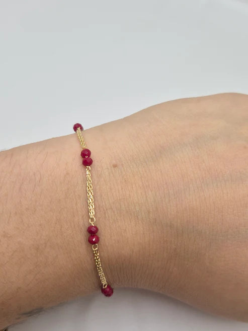 Gold bracelet with red beads on a wrist against a light background available on the TX.ORO website.