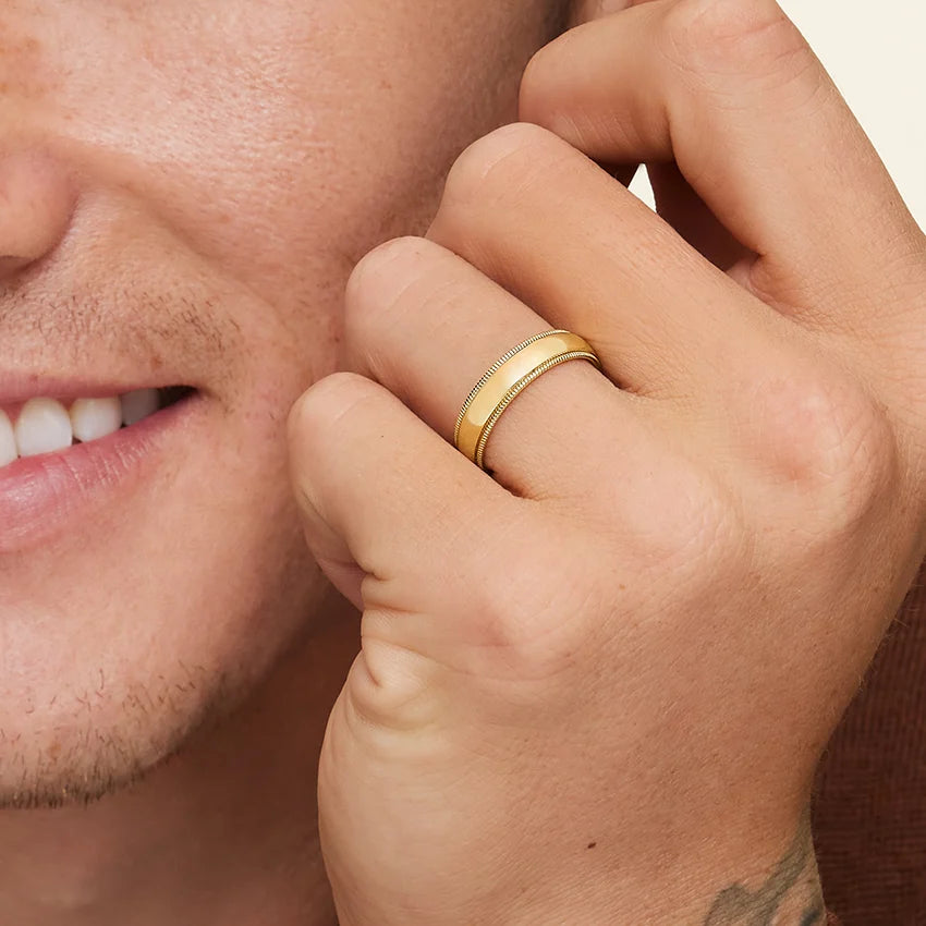 Man wearing a gold ring on his finger with a neutral background