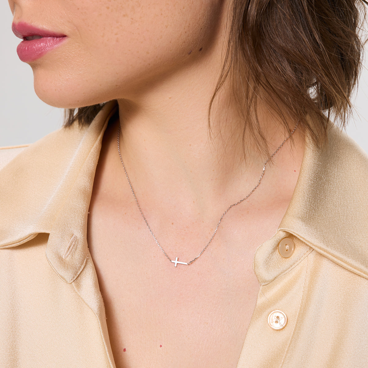 Close-up of a person wearing a delicate necklace with a cross pendant available on the TX.ORO website.