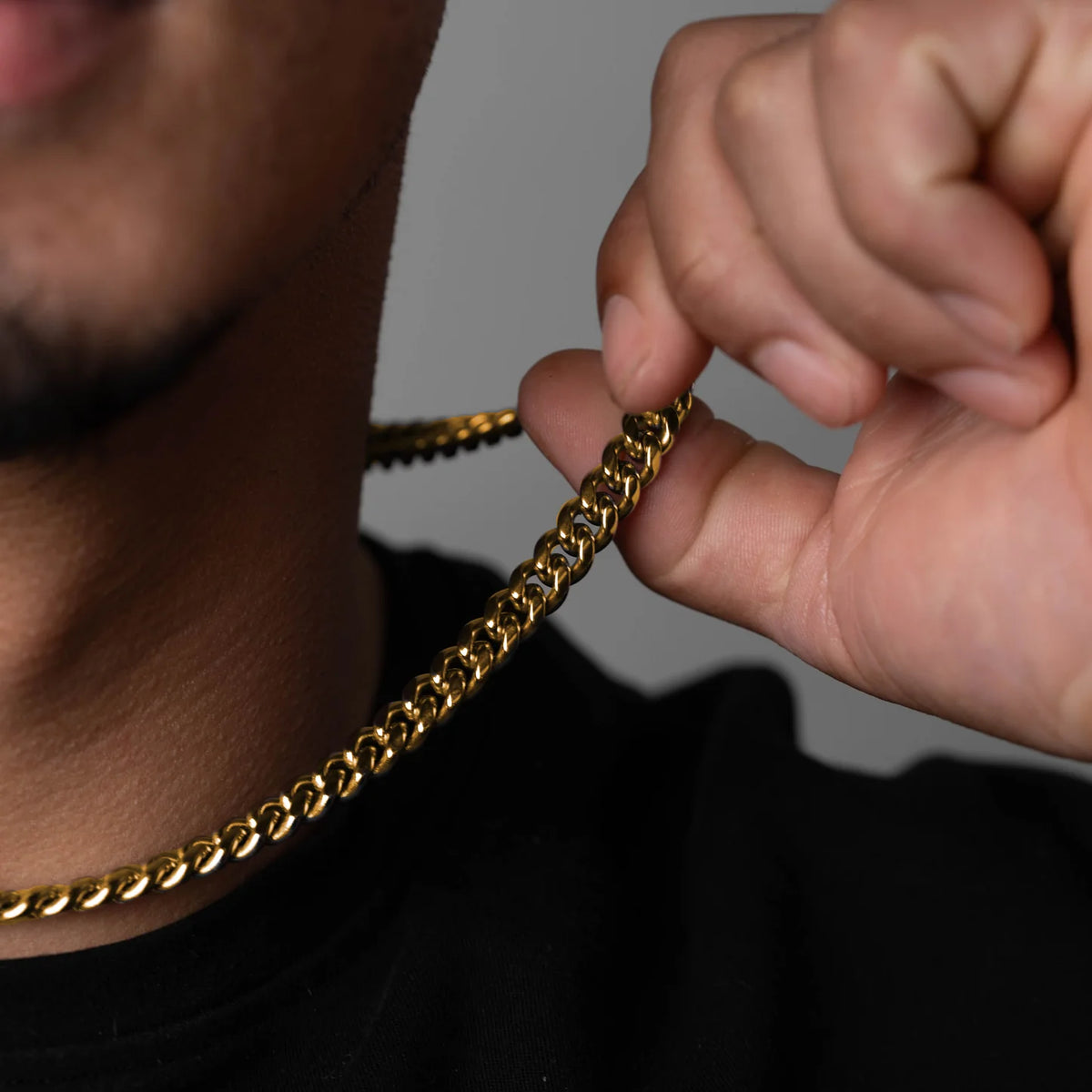 Person wearing a gold chain necklace with a hand adjusting it against a neutral background available on the TX.ORO website.