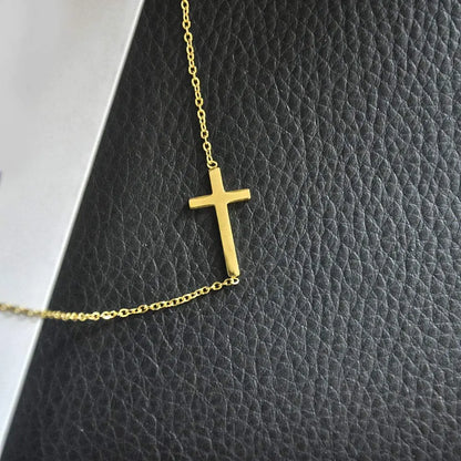 Gold cross necklace on a textured black surface available on the TX.ORO website.