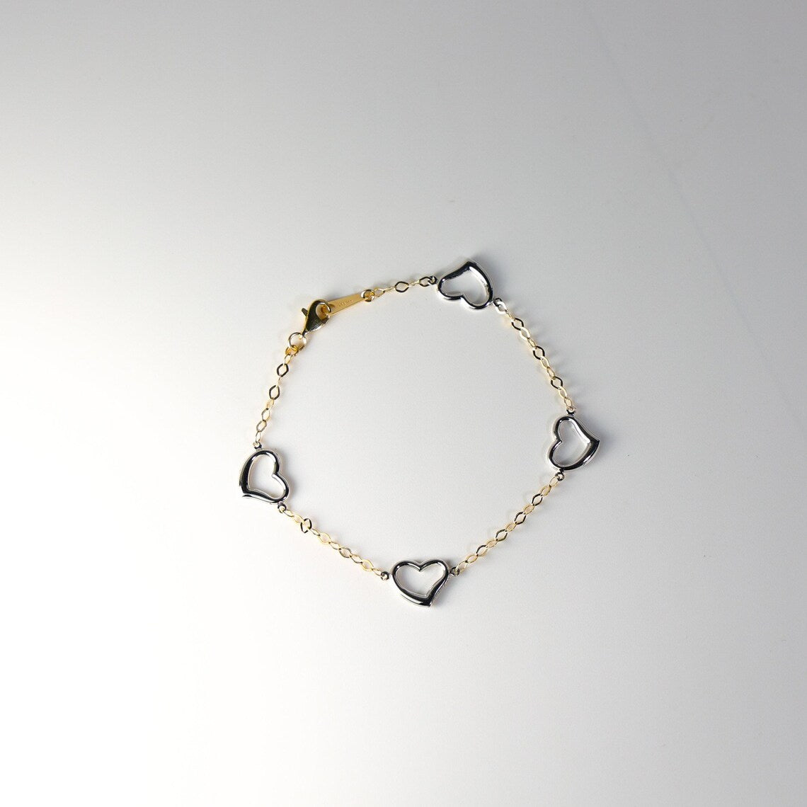 Bracelet with heart-shaped charms on a light gray background available on the TX.ORO website.