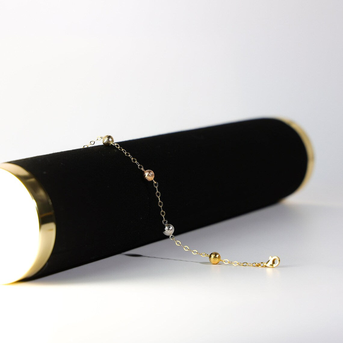 Gold bracelet on a black cylindrical stand with a white background available on the TX.ORO website.