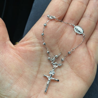 Silver rosary held in a hand against a neutral background availabe on TX.ORO website.