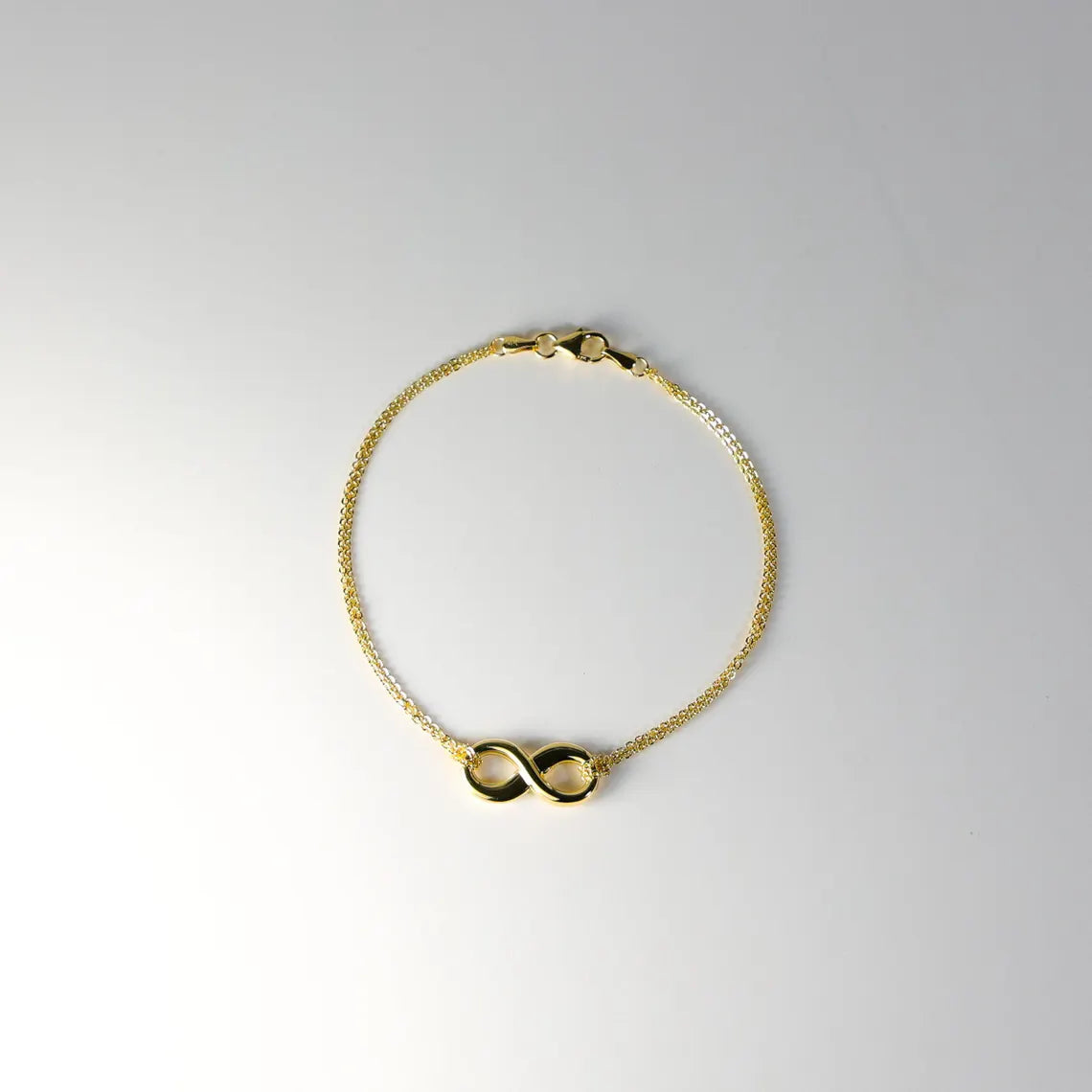 Gold bracelet with a double infinity symbol on a light gray background available on the TX.ORO website.