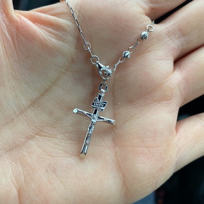 Silver rosary necklace with a crucifix pendant held in a hand availabe on TX.ORO website.