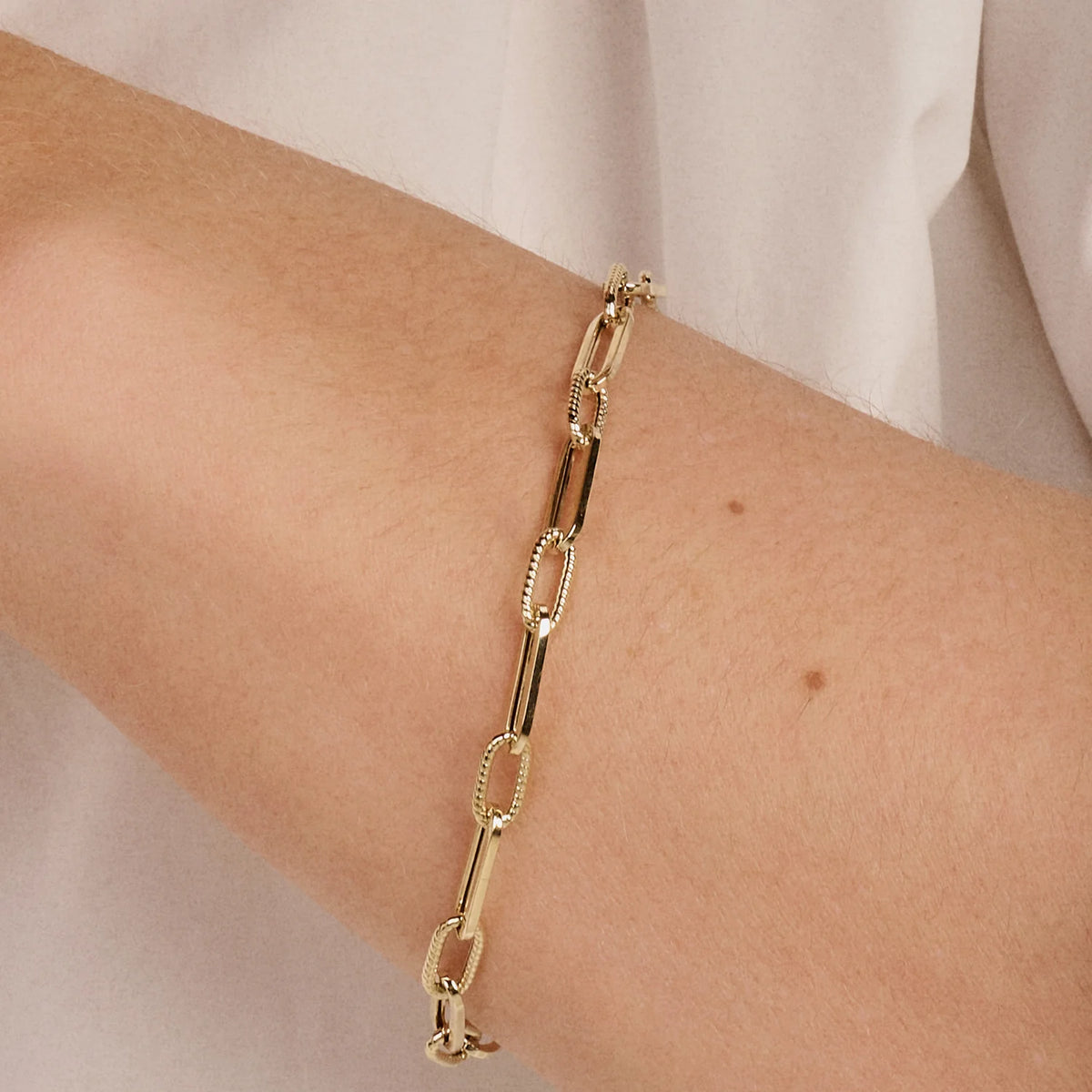 Gold chain bracelet on a person's wrist with a plain background available on the TX.ORO website.