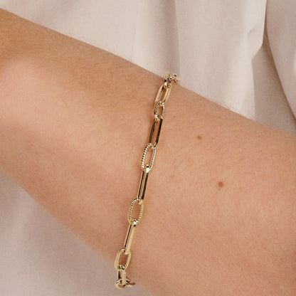 Gold chain bracelet on a person's wrist with a plain background available on the TX.ORO website.