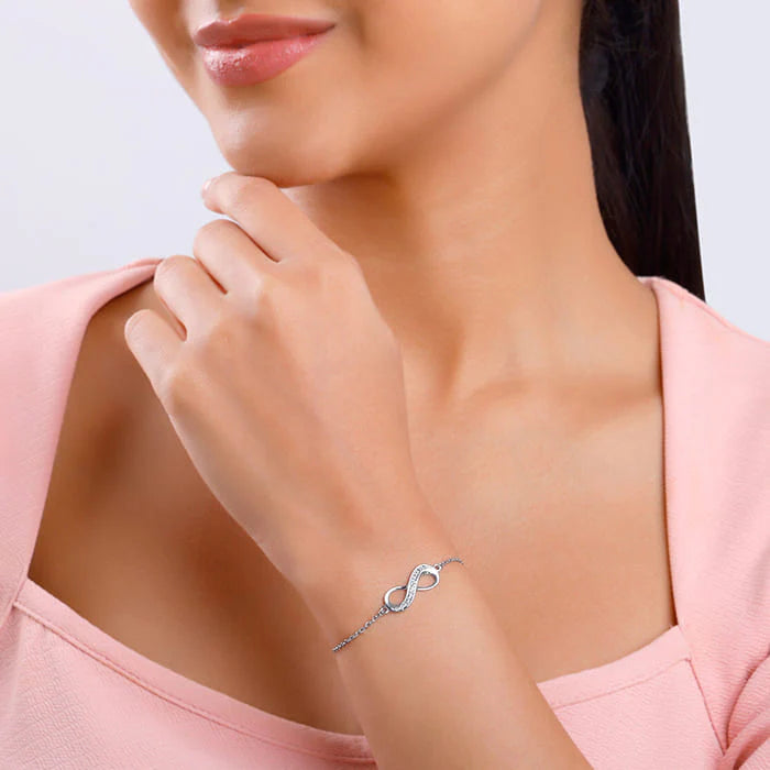 Woman wearing a silver bracelet with an infinity symbol on a light pink background available on the TX.ORO website.