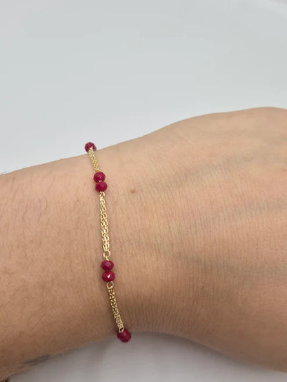 Gold bracelet with red beads on a wrist against a light background available on the TX.ORO website.