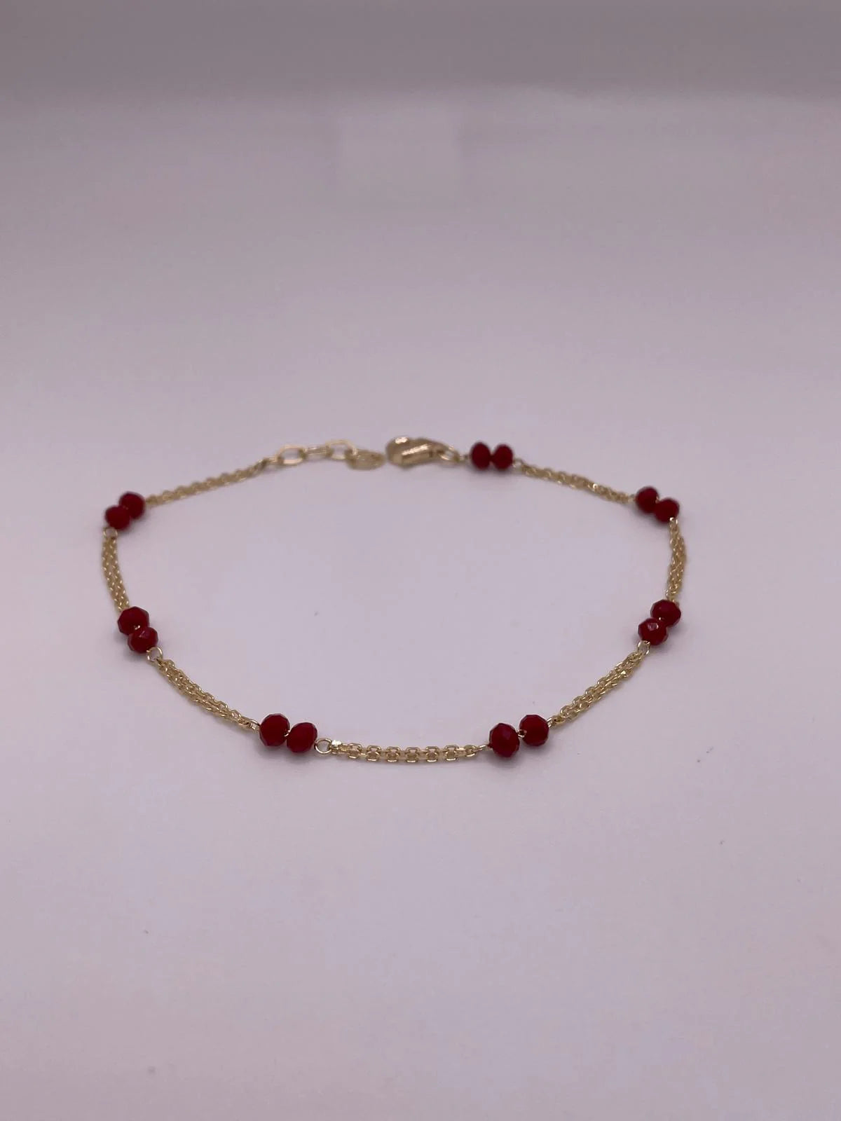 Gold bracelet with red beads on a light gray background available on the TX.ORO website.