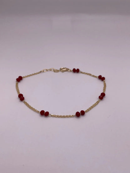 Gold bracelet with red beads on a light gray background available on the TX.ORO website.
