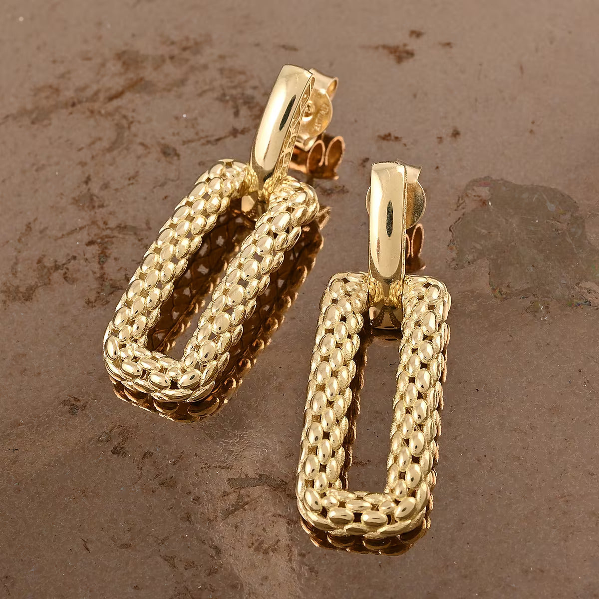 Pair of gold hoop earrings on a textured brown surface available on the TX.ORO website.