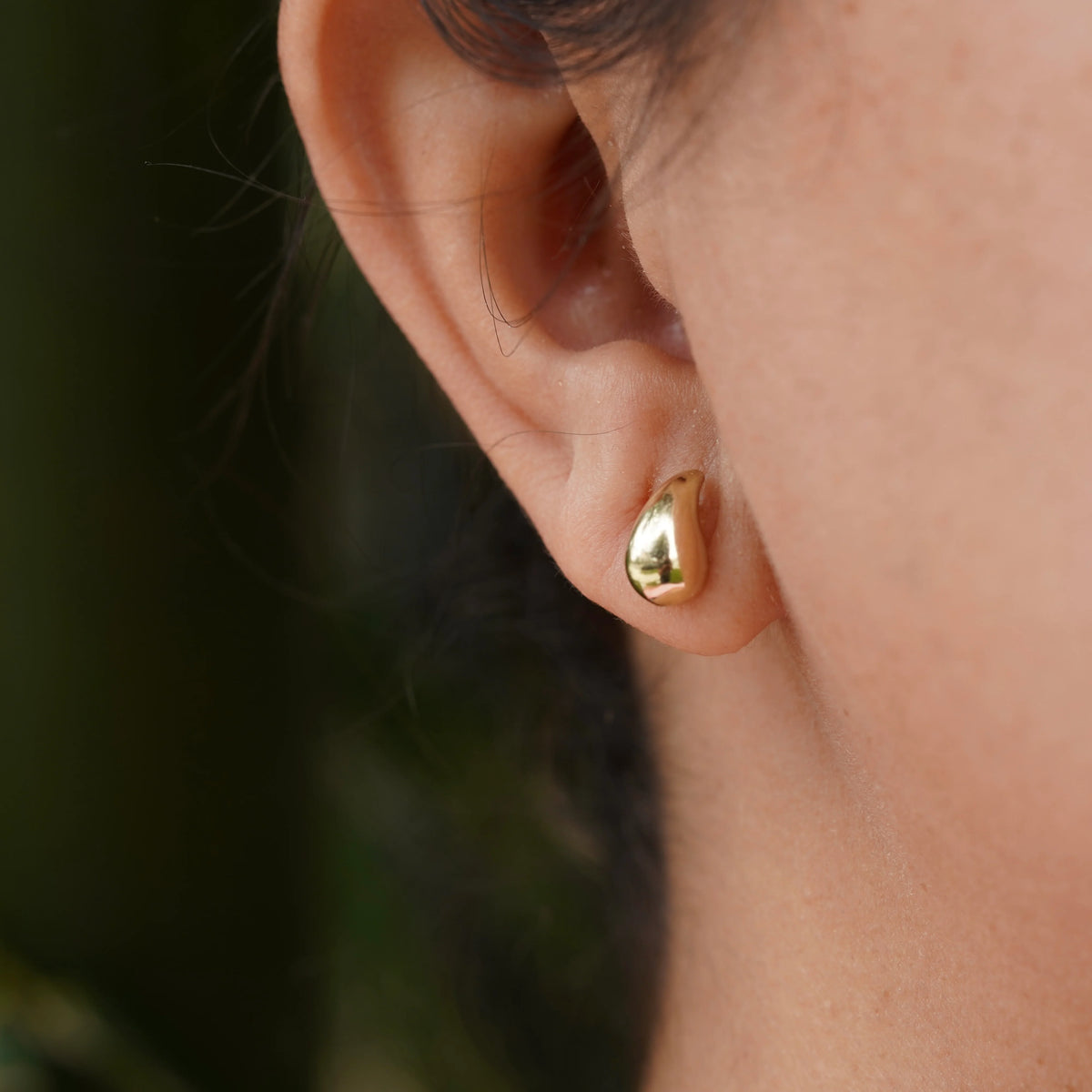 Close-up of a person wearing a gold earring with a blurred background available on the TX.ORO website.