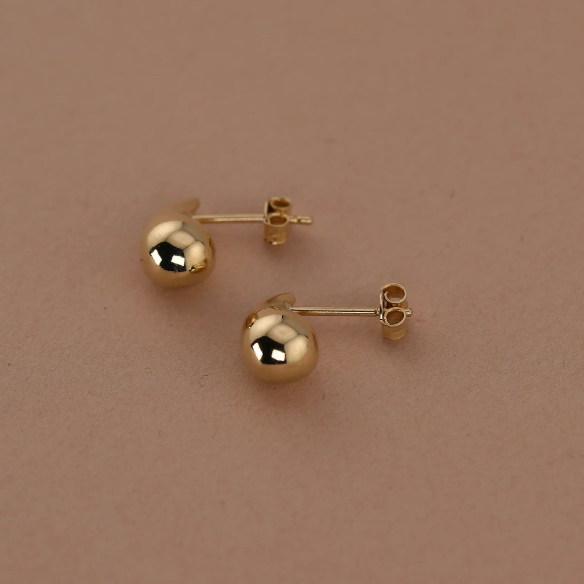 Gold ball earrings on a beige background available on the TX.ORO website.