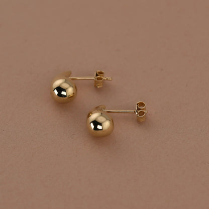 Gold ball earrings on a beige background available on the TX.ORO website.