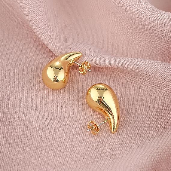 Gold earrings on a pink fabric background available on the TX.ORO website.