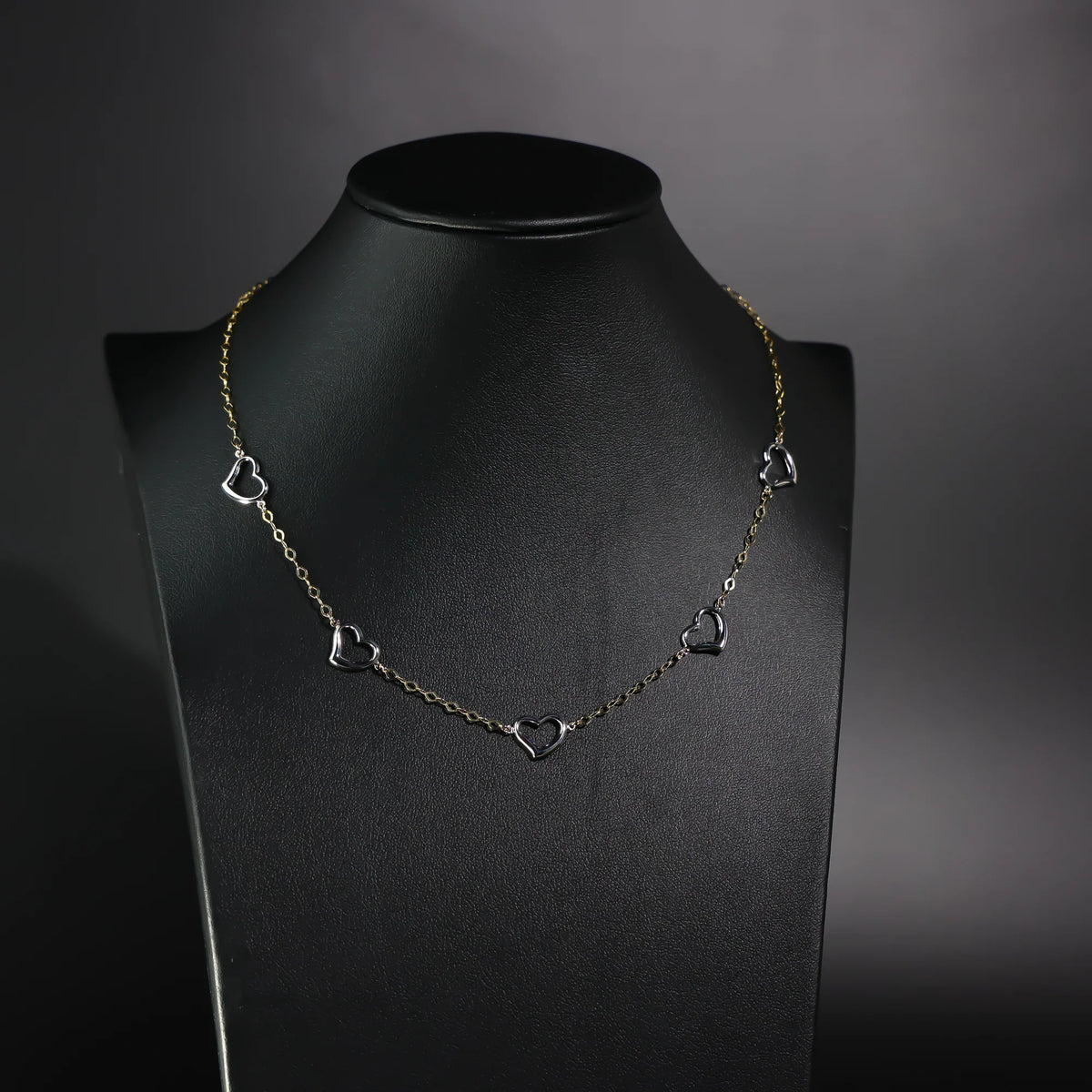Necklace with heart-shaped pendants on a black mannequin against a dark background available on the TX.ORO website.