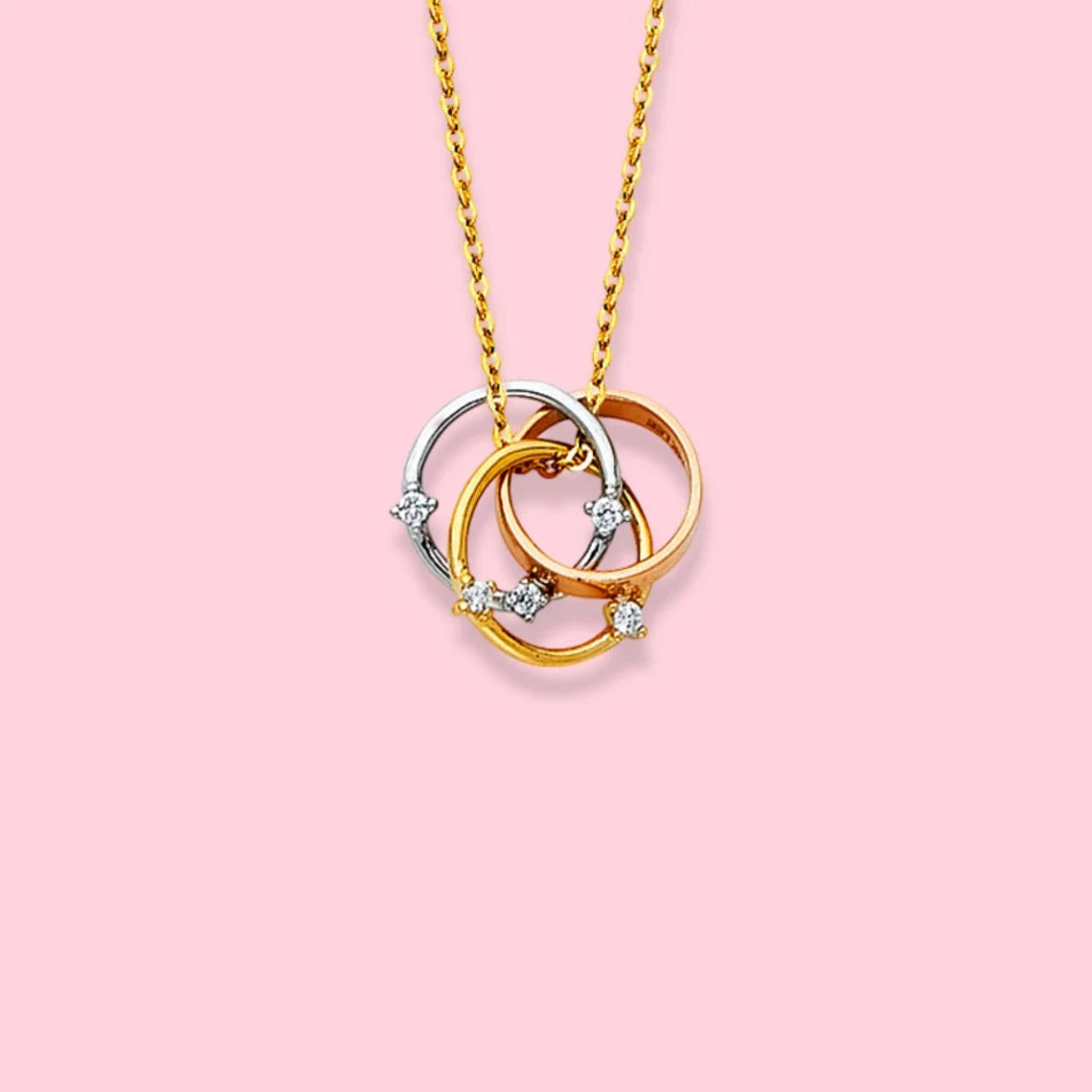 Three interlocking circular pendants on a gold chain against a pink background available on the TX.ORO website.