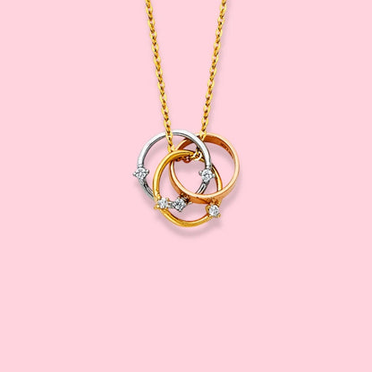 Three interlocking circular pendants on a gold chain against a pink background available on the TX.ORO website.