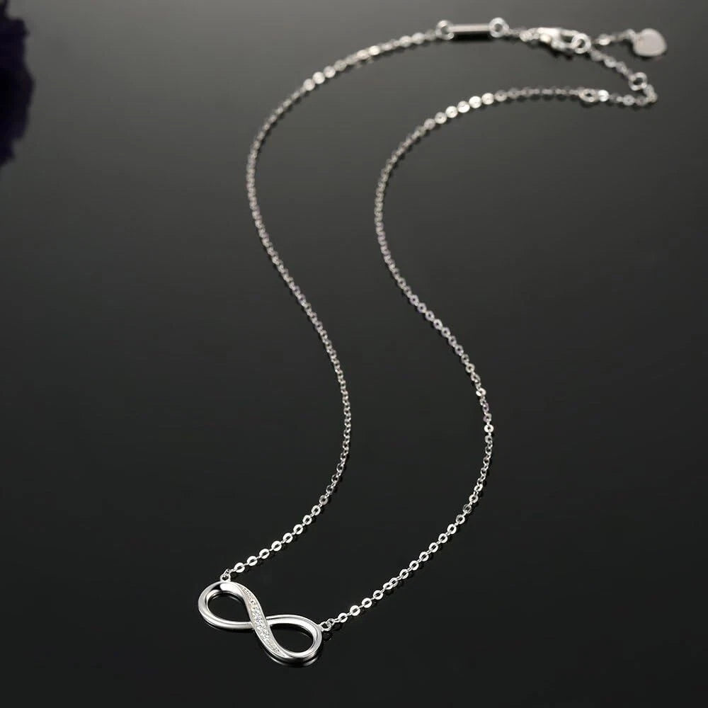 Silver infinity necklace on a dark background available on the TX.ORO website.