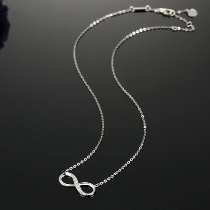 Silver infinity necklace on a dark background available on the TX.ORO website.