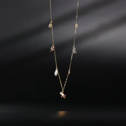 Delicate gold necklace with small pendants on a dark background available on the TX.ORO website.