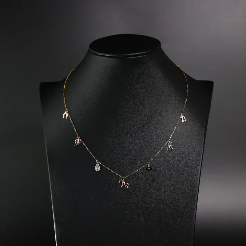 Necklace with small pendants on a black mannequin against a dark background available on the TX.ORO website.