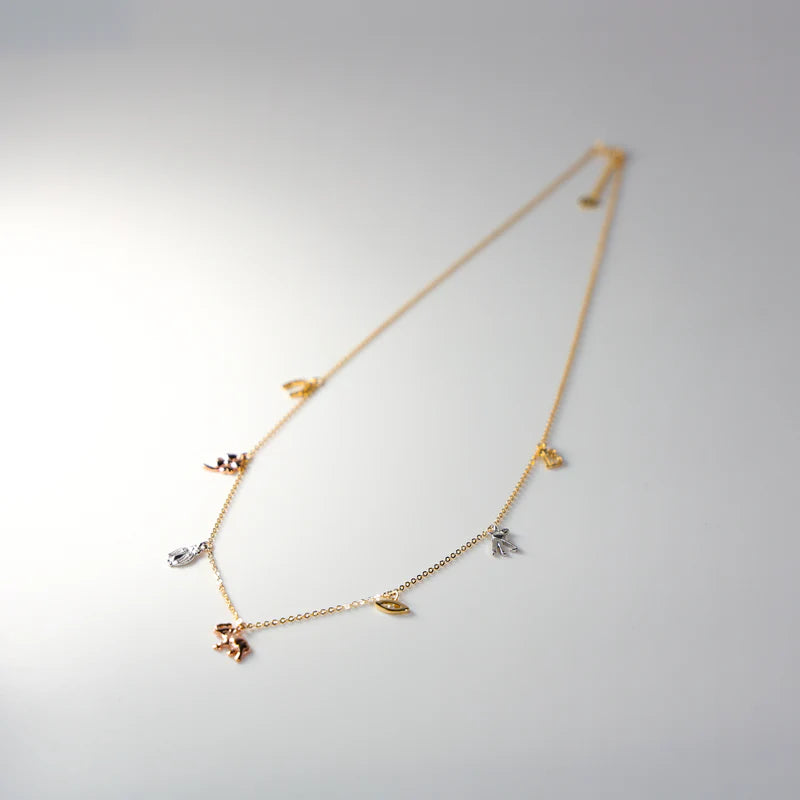 Delicate gold necklace with small charms on a light gray background available on the TX.ORO website.