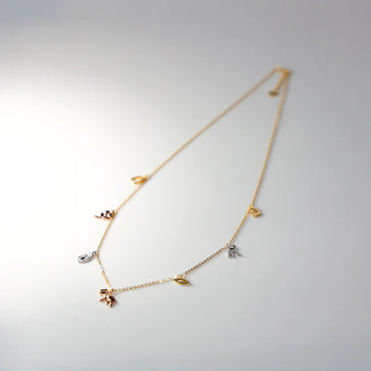 Delicate gold necklace with small charms on a light gray background available on the TX.ORO website.