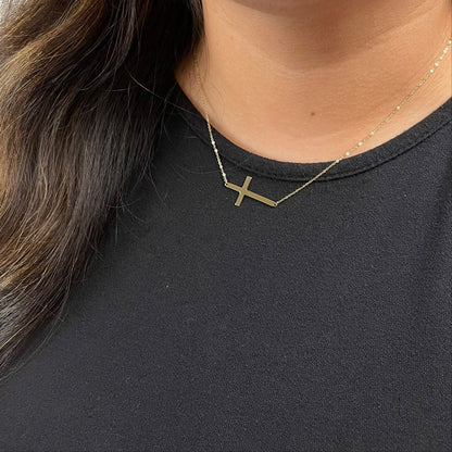 Gold cross necklace on a person wearing a black shirt available on the TX.ORO website.