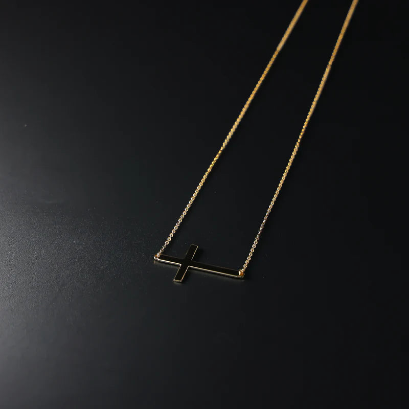 Gold necklace with a cross pendant on a black background available on the TX.ORO website.