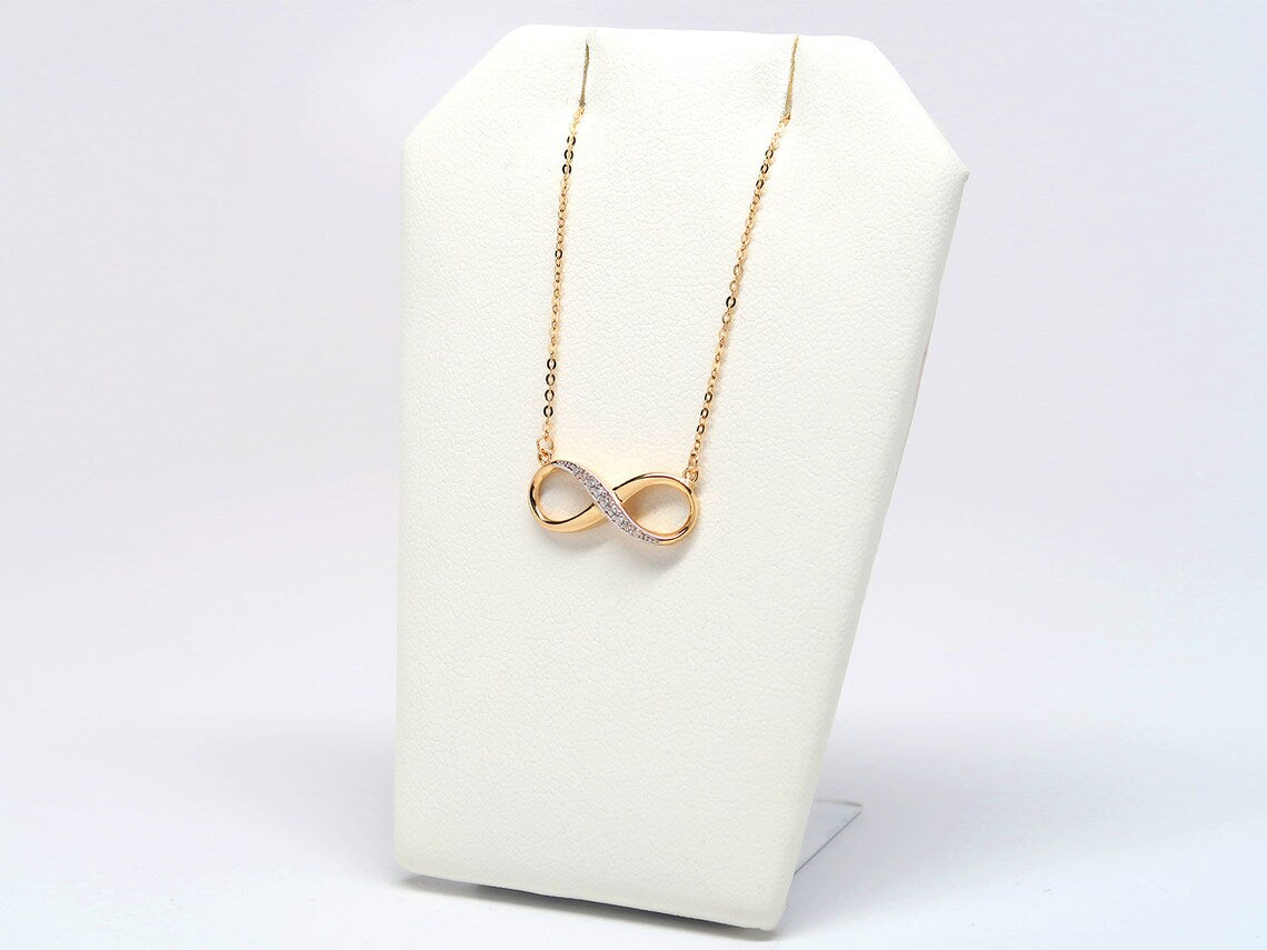 Gold infinity necklace on a white jewelry display stand available on the TX.ORO website.