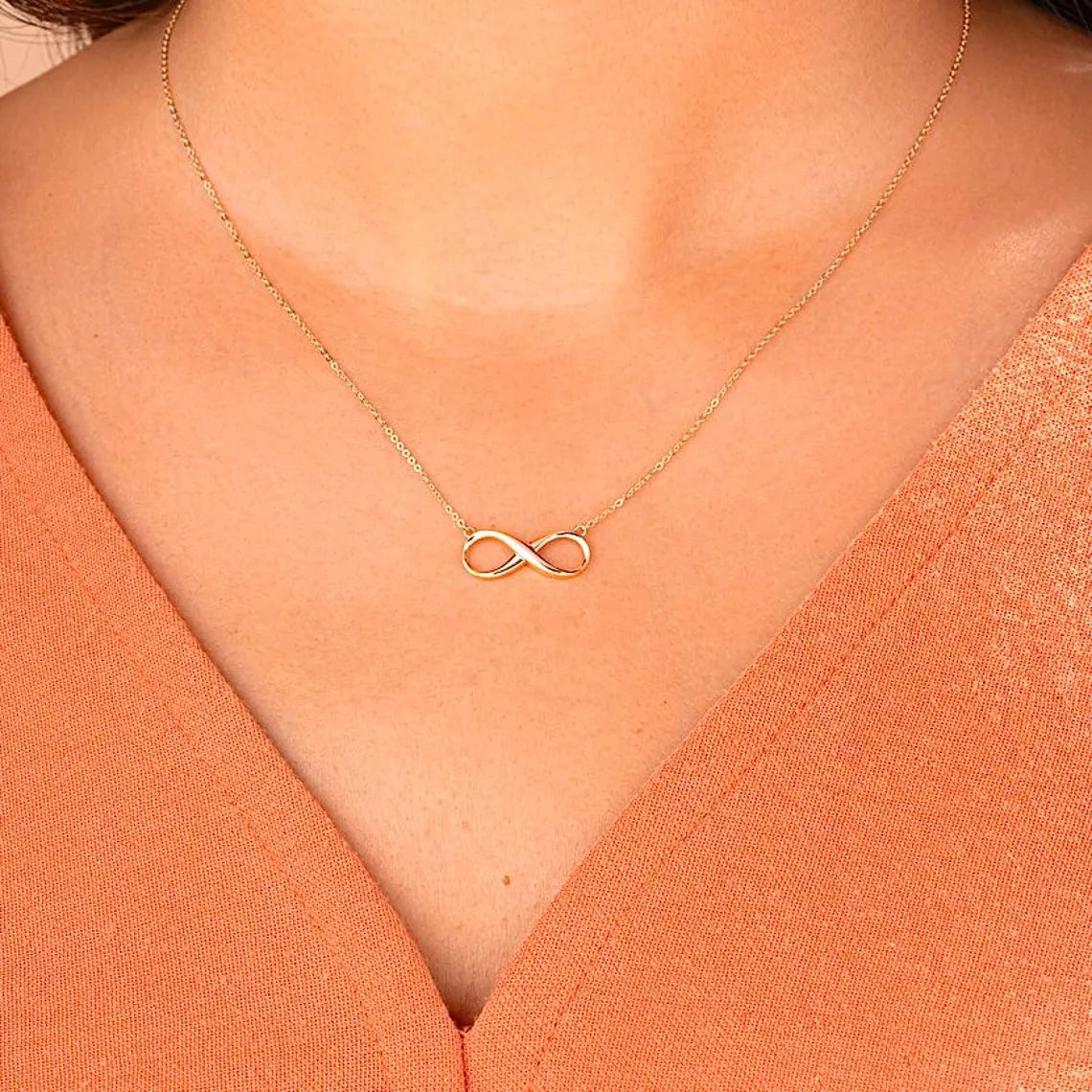 Gold infinity necklace on a person wearing an orange top available on the TX.ORO website.