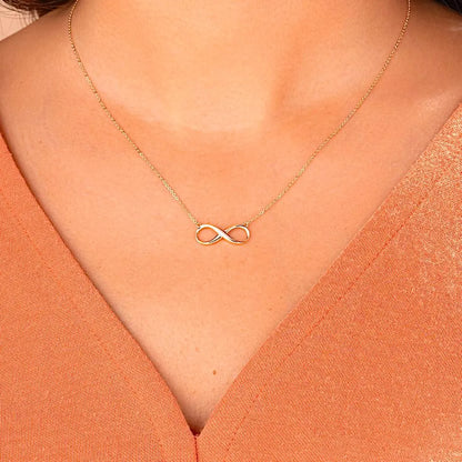 Gold infinity necklace on a person wearing an orange top available on the TX.ORO website.