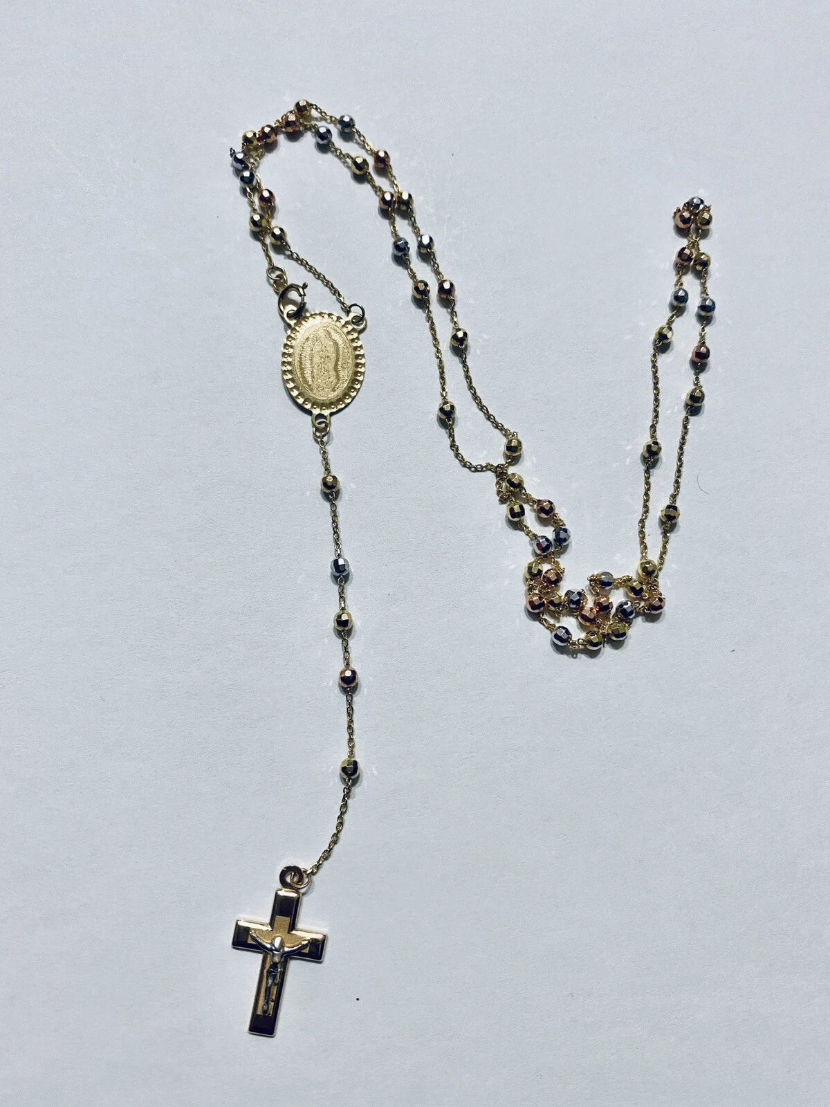 Rosary necklace with beads and a cross on a light gray background availabe on TX.ORO website.