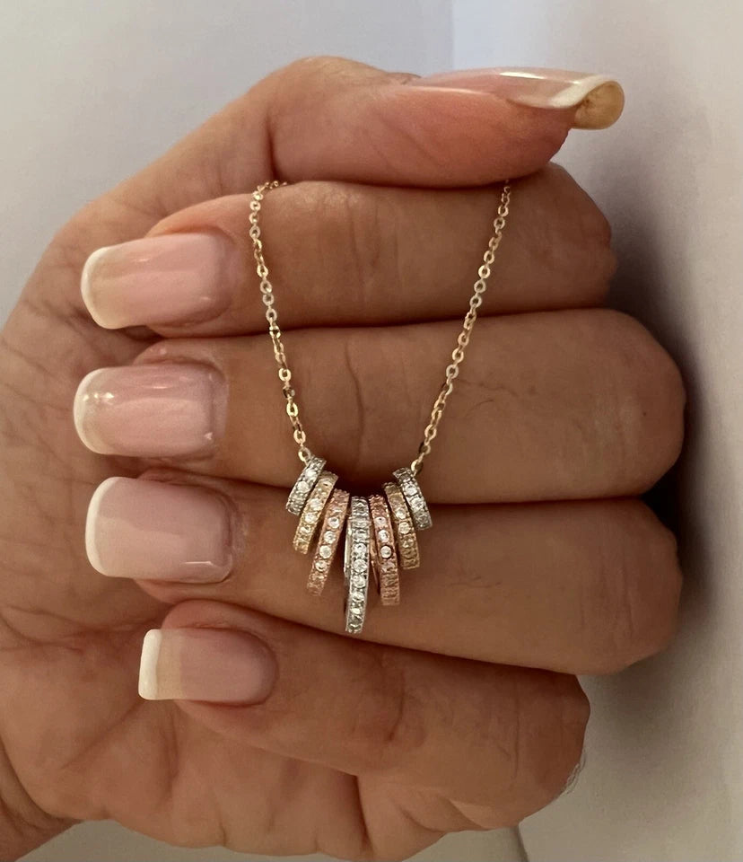 Gold necklace with diamond pendants held by a hand against a neutral background available on the TX.ORO website.