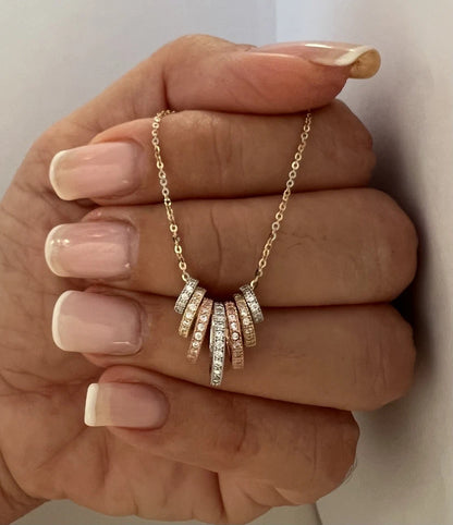 Gold necklace with diamond pendants held by a hand against a neutral background available on the TX.ORO website.