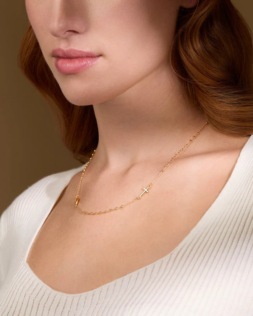 Close-up of a person wearing a gold necklace with a cross pendant on a neutral background available on the TX.ORO website.