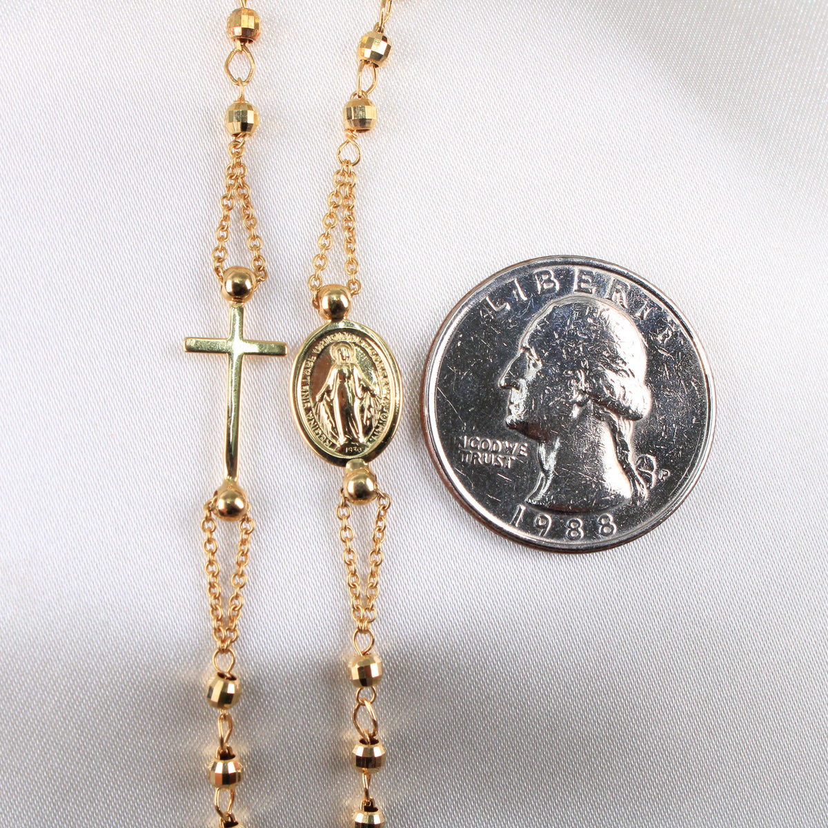 Gold rosary with a cross and medal next to a quarter on a white background available on the TX.ORO website.