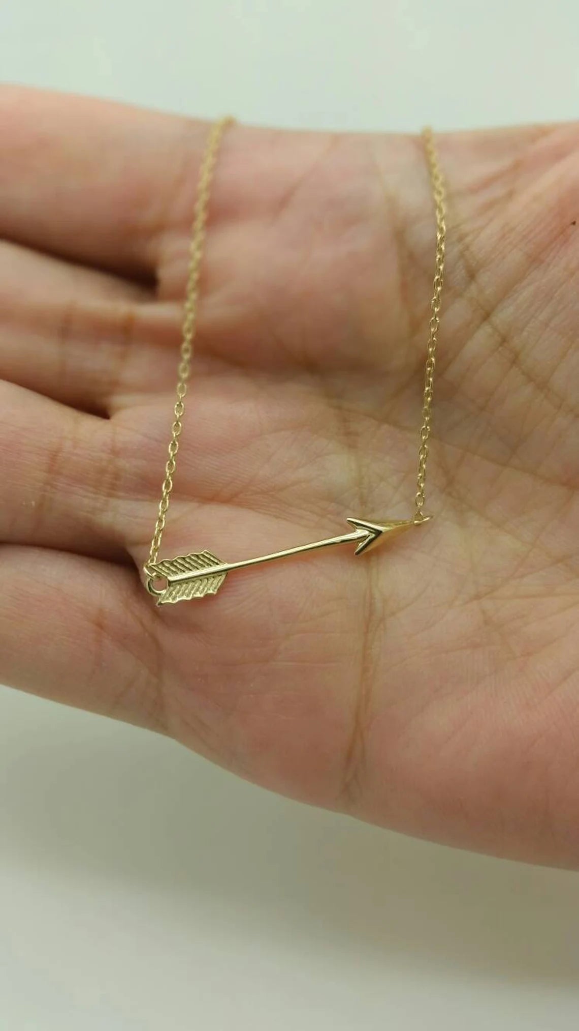 Gold arrow necklace on a hand against a plain background available on the TX.ORO website.