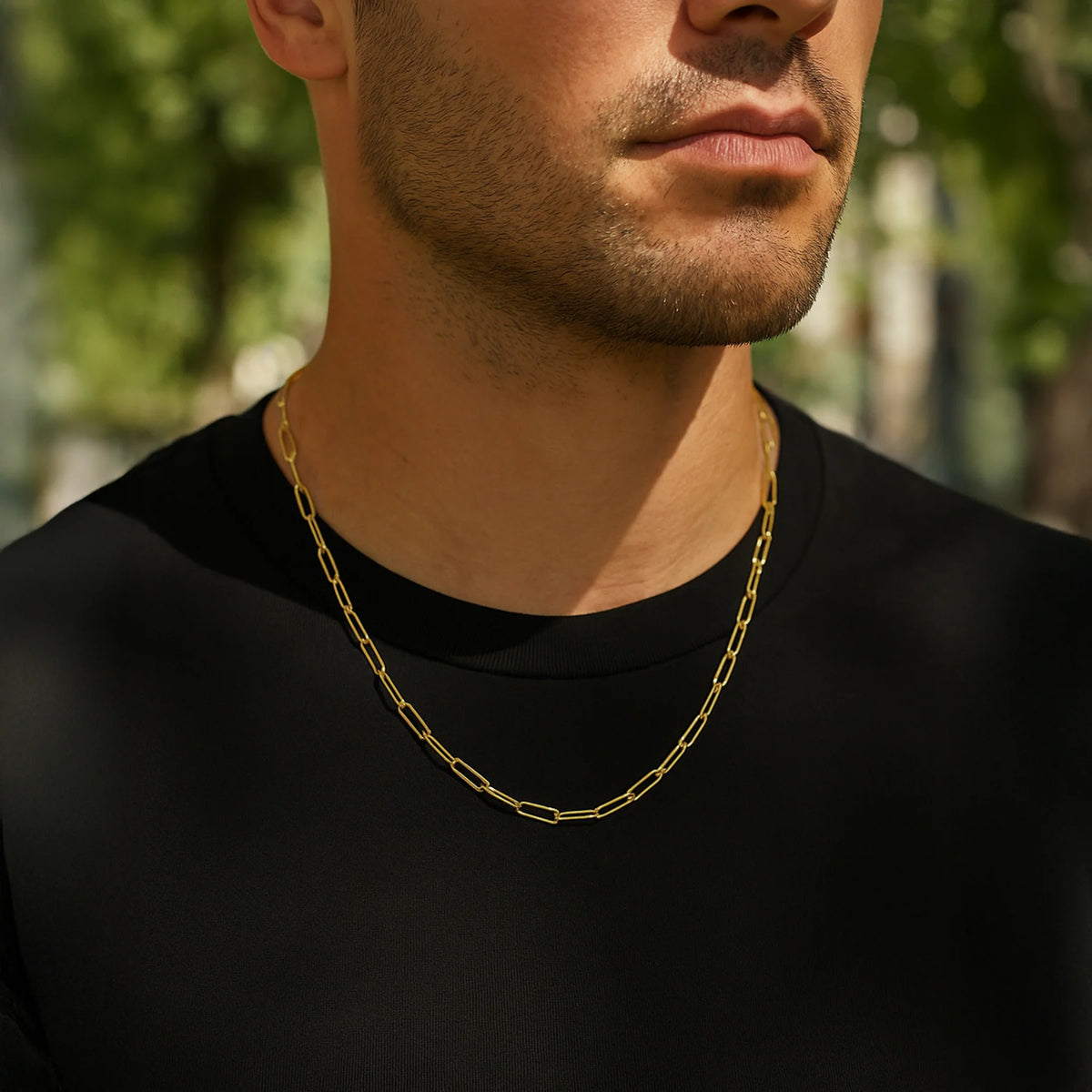 Man wearing a gold chain necklace with a blurred green outdoor  background available on the TX.ORO website.