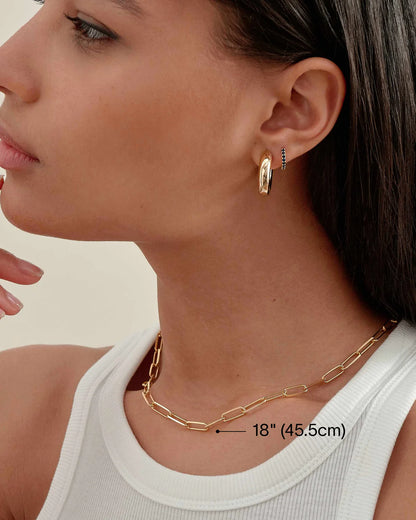Close-up of a person wearing gold hoop earrings and a gold chain necklace with measurement label available on the TX.ORO website..
