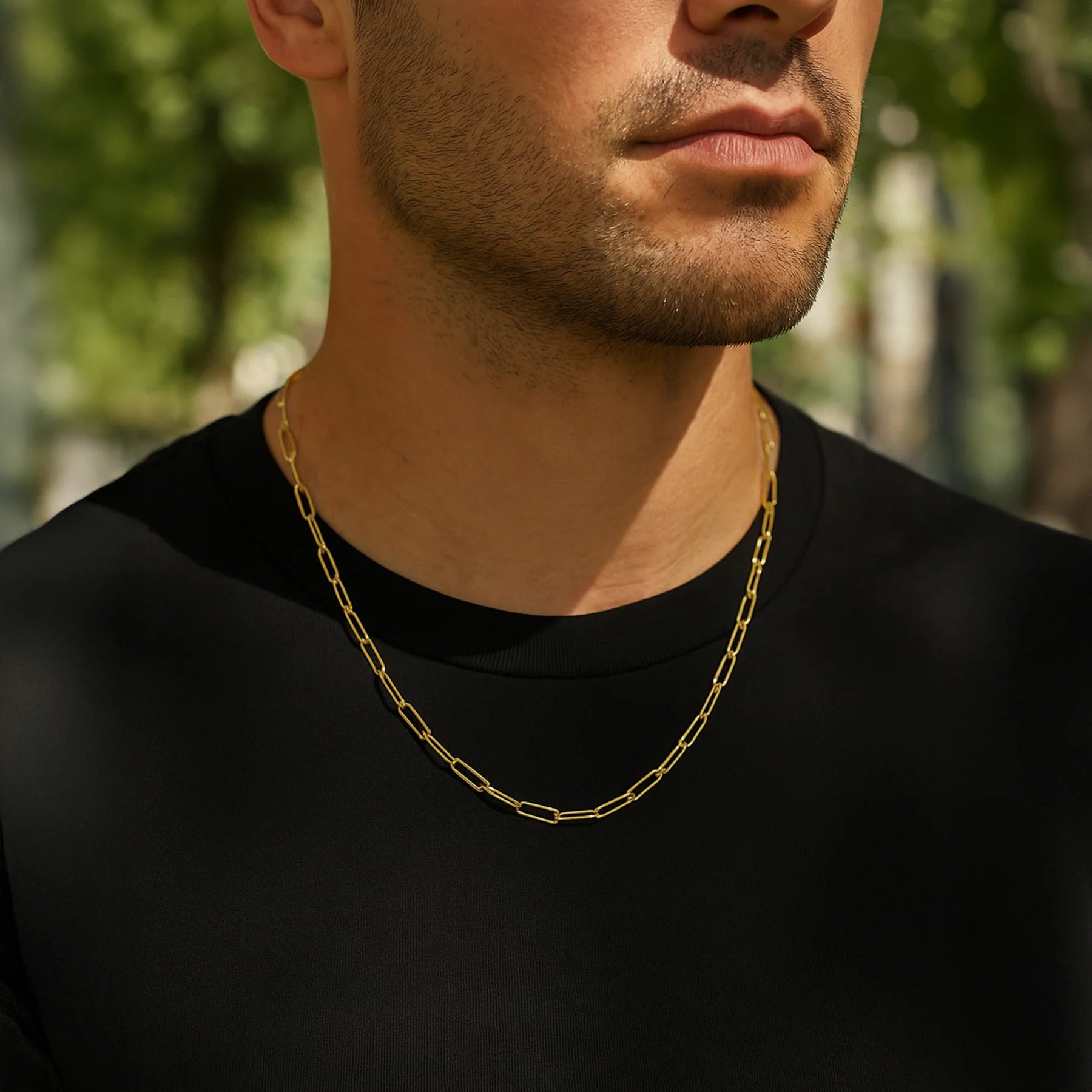 Man wearing a gold chain necklace with a blurred green outdoor background available on the TX.ORO website.