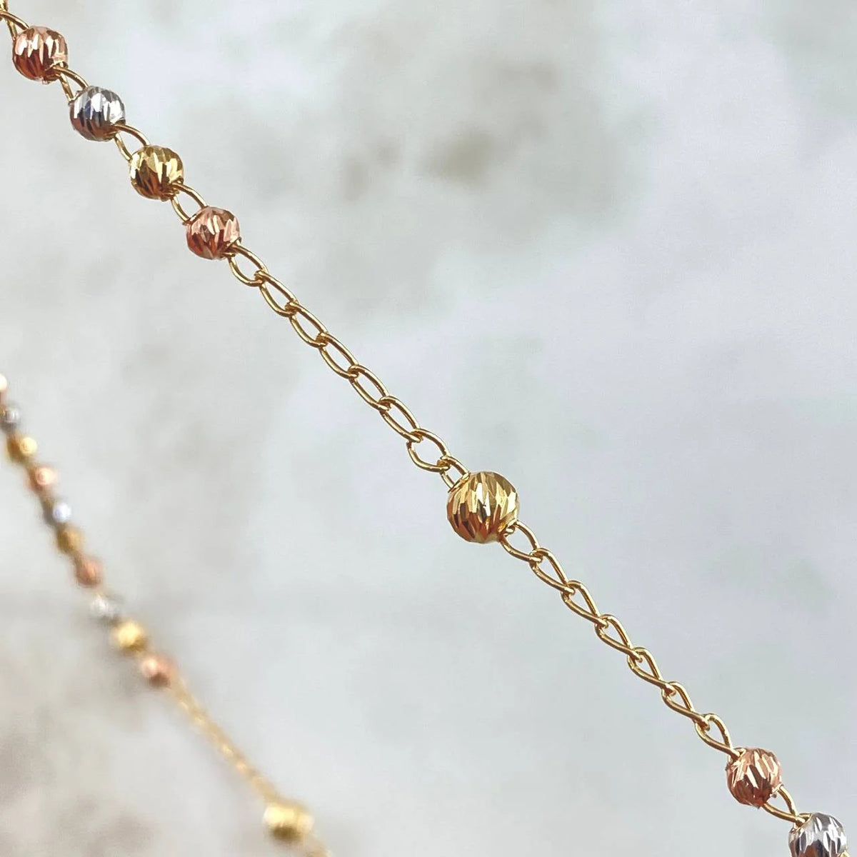 Close-up of a gold chain with small beads on a blurred background available on the TX.ORO website.