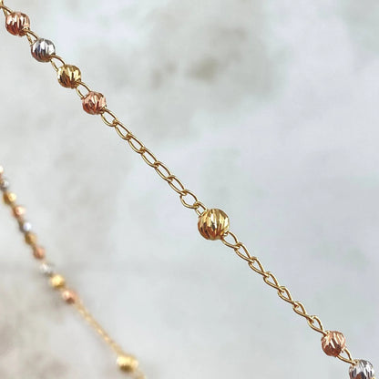 Close-up of a gold chain with small beads on a blurred background available on the TX.ORO website.