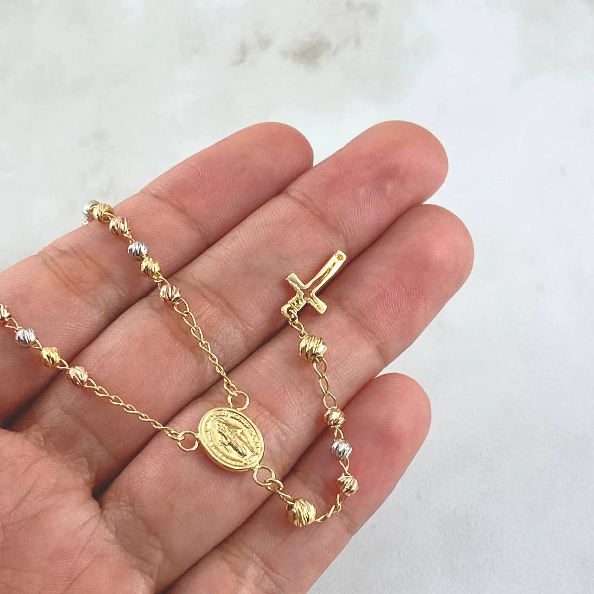Gold bracelet with a religious charm on a hand against a white background available on the TX.ORO website.
