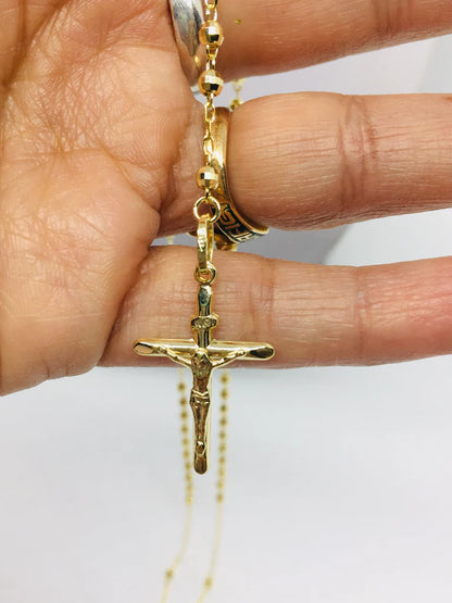 Gold crucifix necklace held by a hand on a white background available on the TX.ORO website.