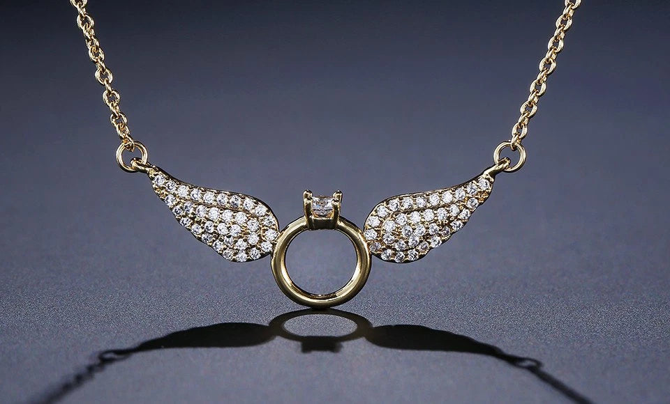Gold necklace with angel wing pendants on a dark background available on the TX.ORO website.